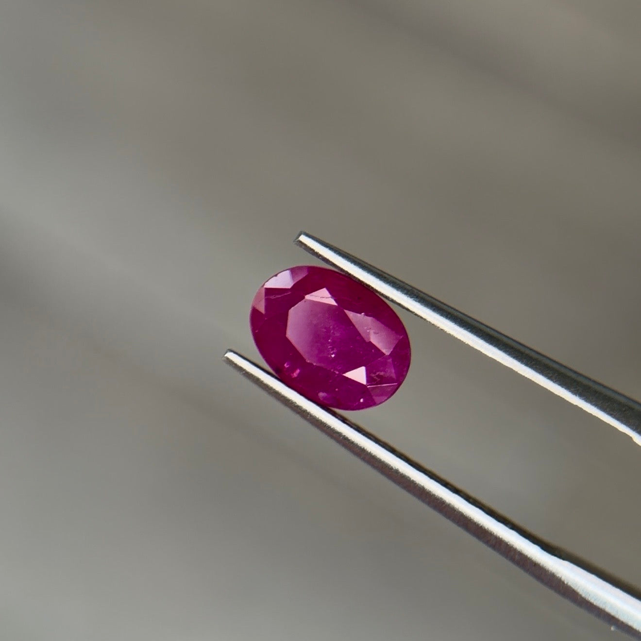 Oval mixed-cut heated Burmese ruby in a medium-dark purplish red with strong saturation, held face-up in steel tweezers at Sapphire Row - the 15th and 40th anniversary gemstone