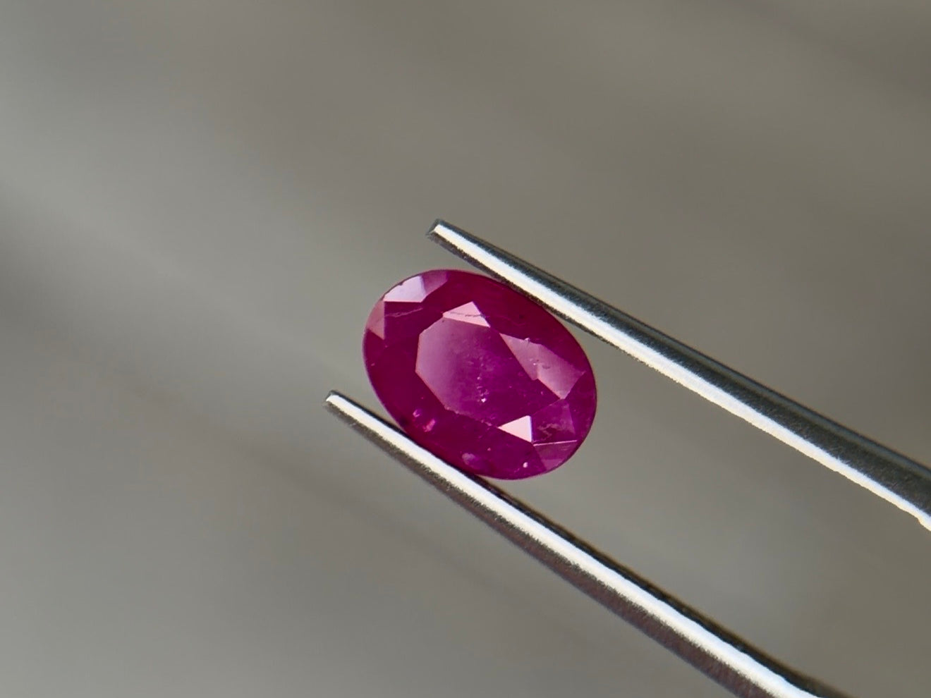 Oval mixed-cut heated Burmese ruby in a medium-dark purplish red with strong saturation, held face-up in steel tweezers at Sapphire Row - the 15th and 40th anniversary gemstone