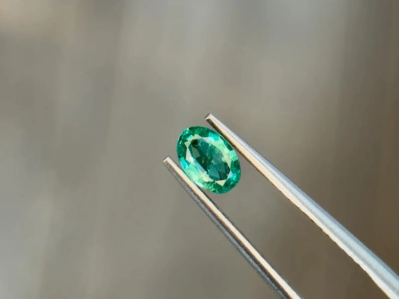 Vivid green oval-cut natural emerald held in jeweler's tweezers, an example of investment-grade color at Sapphire Row