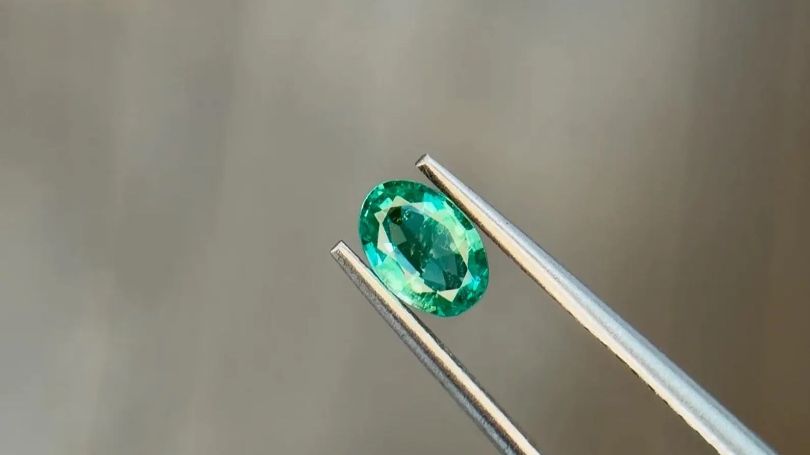 Vivid green oval-cut natural emerald held in jeweler's tweezers, an example of investment-grade color at Sapphire Row