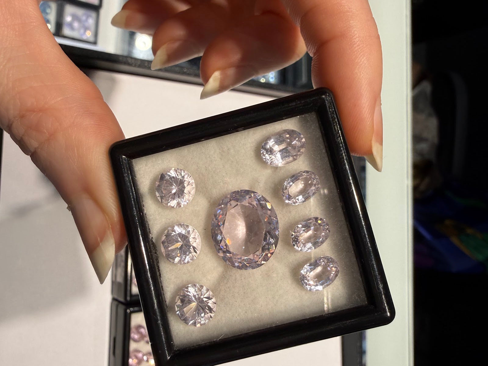 A collector examines a gem box of pastel pink oval and round-cut gemstones at Sapphire Row, the kind of matched parcel prized by colored gemstone collectors