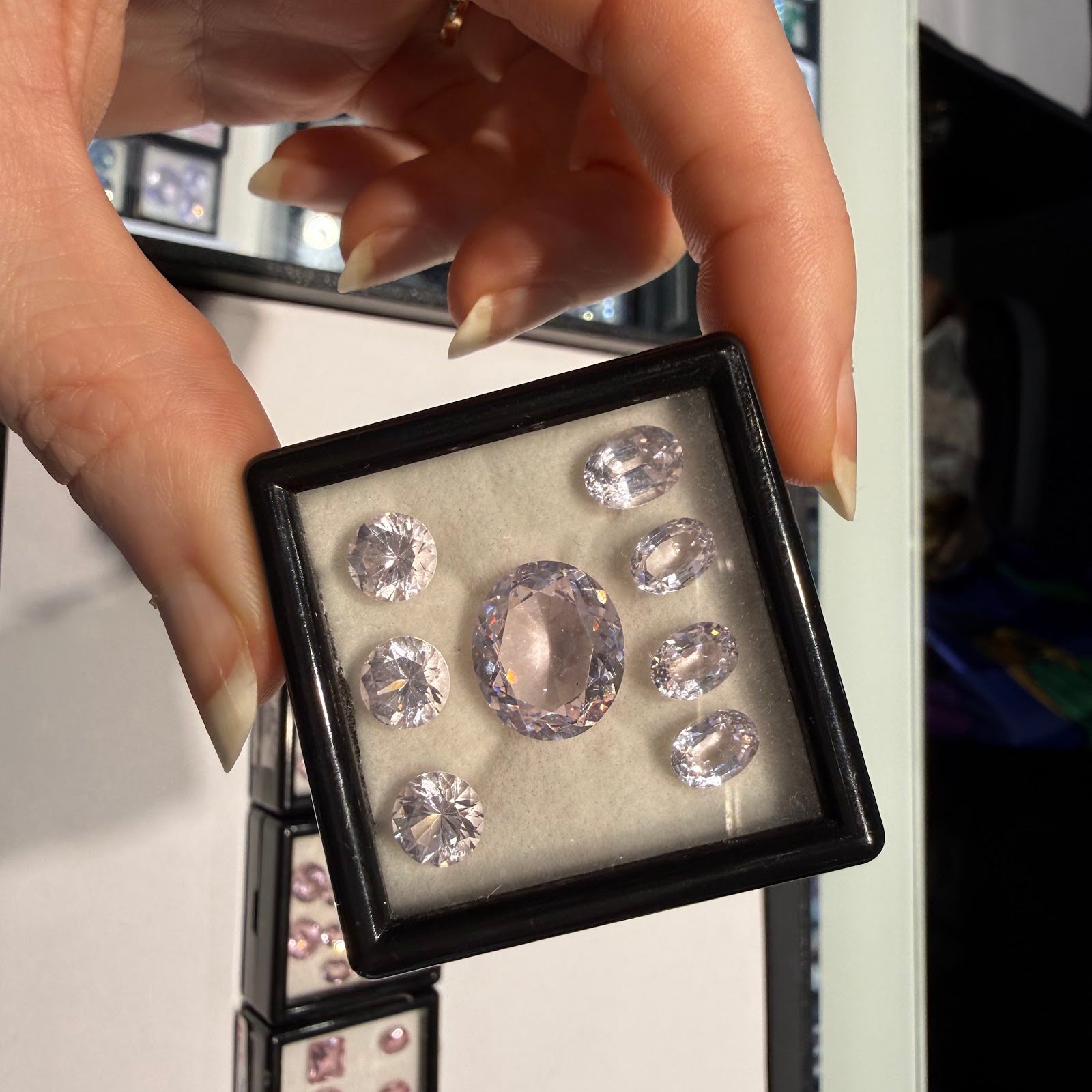A collector examines a gem box of pastel pink oval and round-cut gemstones at Sapphire Row, the kind of matched parcel prized by colored gemstone collectors
