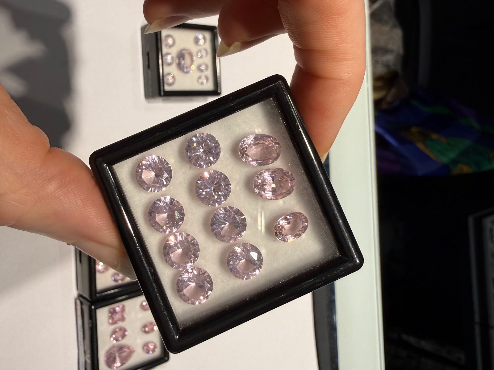 Hand holding a gem box of matched pastel pink oval and round brilliant-cut gemstones at Sapphire Row, an example of the natural colored gemstones discussed in this lab-grown vs natural guide