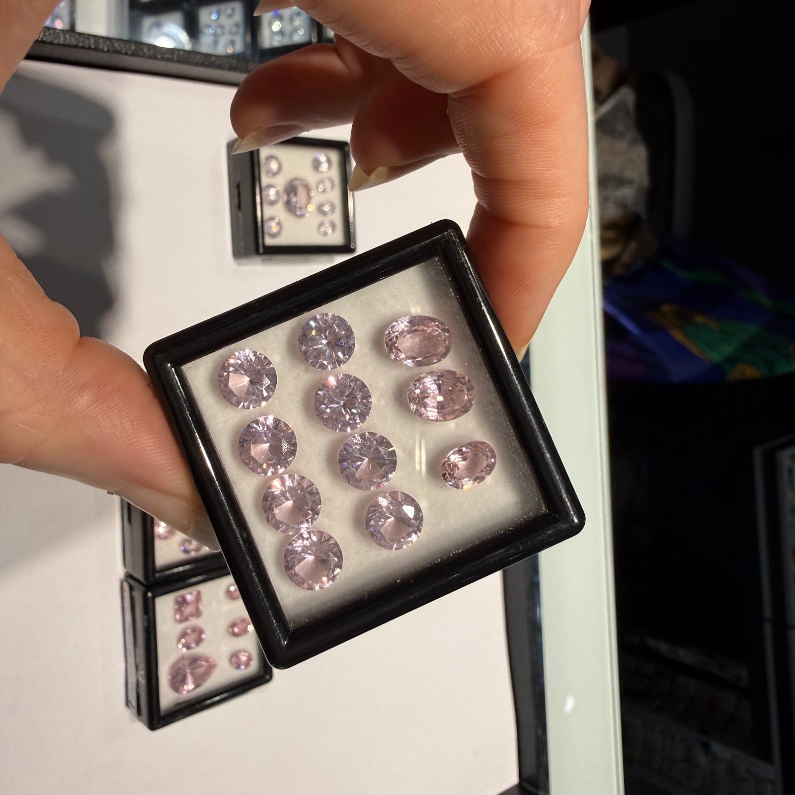 Hand holding a gem box of matched pastel pink oval and round brilliant-cut gemstones at Sapphire Row, an example of the natural colored gemstones discussed in this lab-grown vs natural guide
