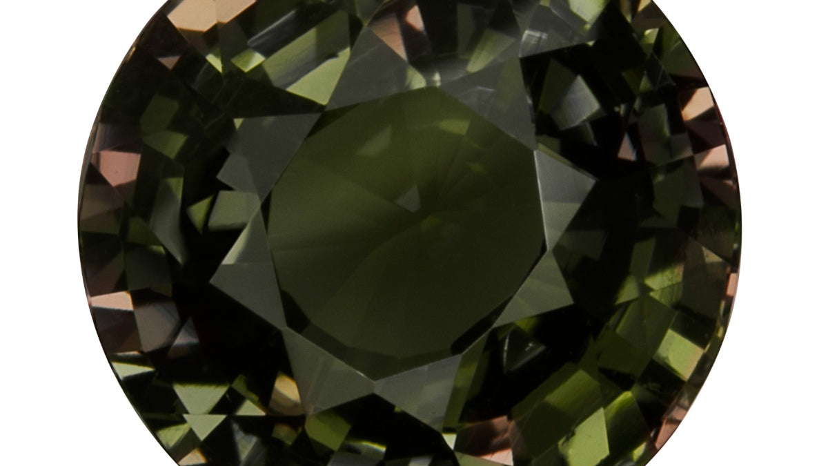 Round brilliant-cut alexandrite from Sri Lanka on a white background, showing a dark grayish olive green body with flashes of brownish pink and orange in the facets