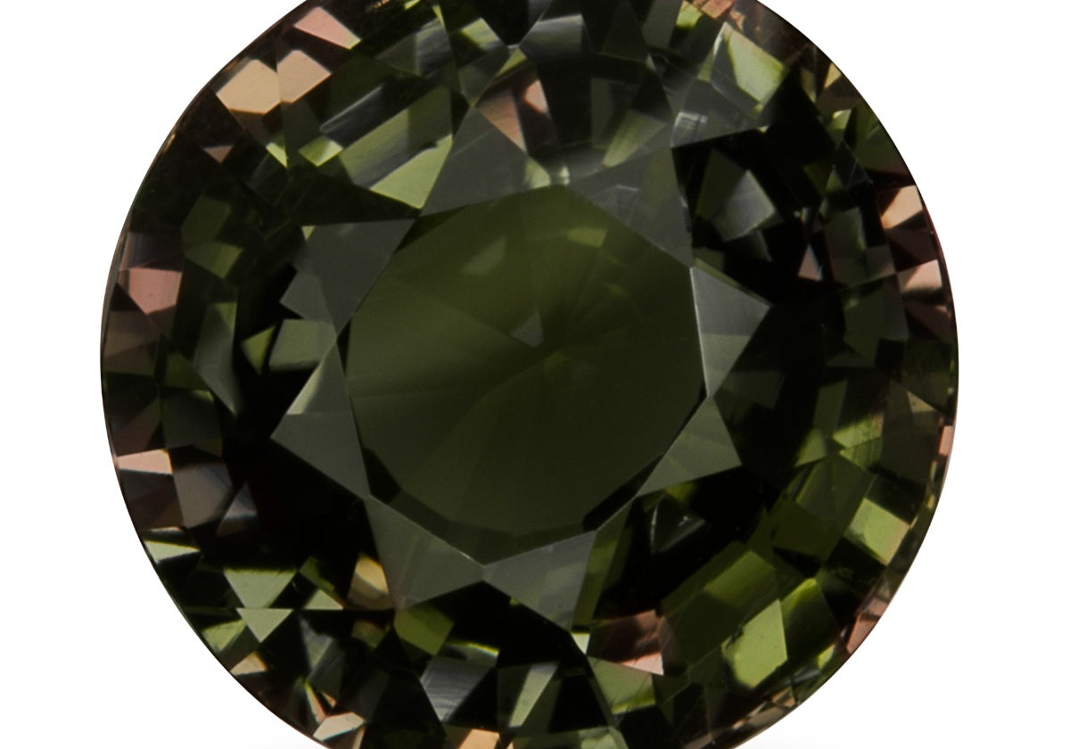 Round brilliant-cut alexandrite from Sri Lanka on a white background, showing a dark grayish olive green body with flashes of brownish pink and orange in the facets