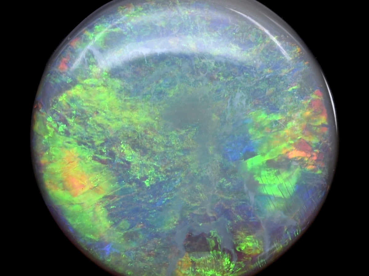 Round precious opal cabochon photographed against black at Sapphire Row, showing vivid green, blue, orange and red play-of-color across a translucent grayish white body - the traditional October birthstone