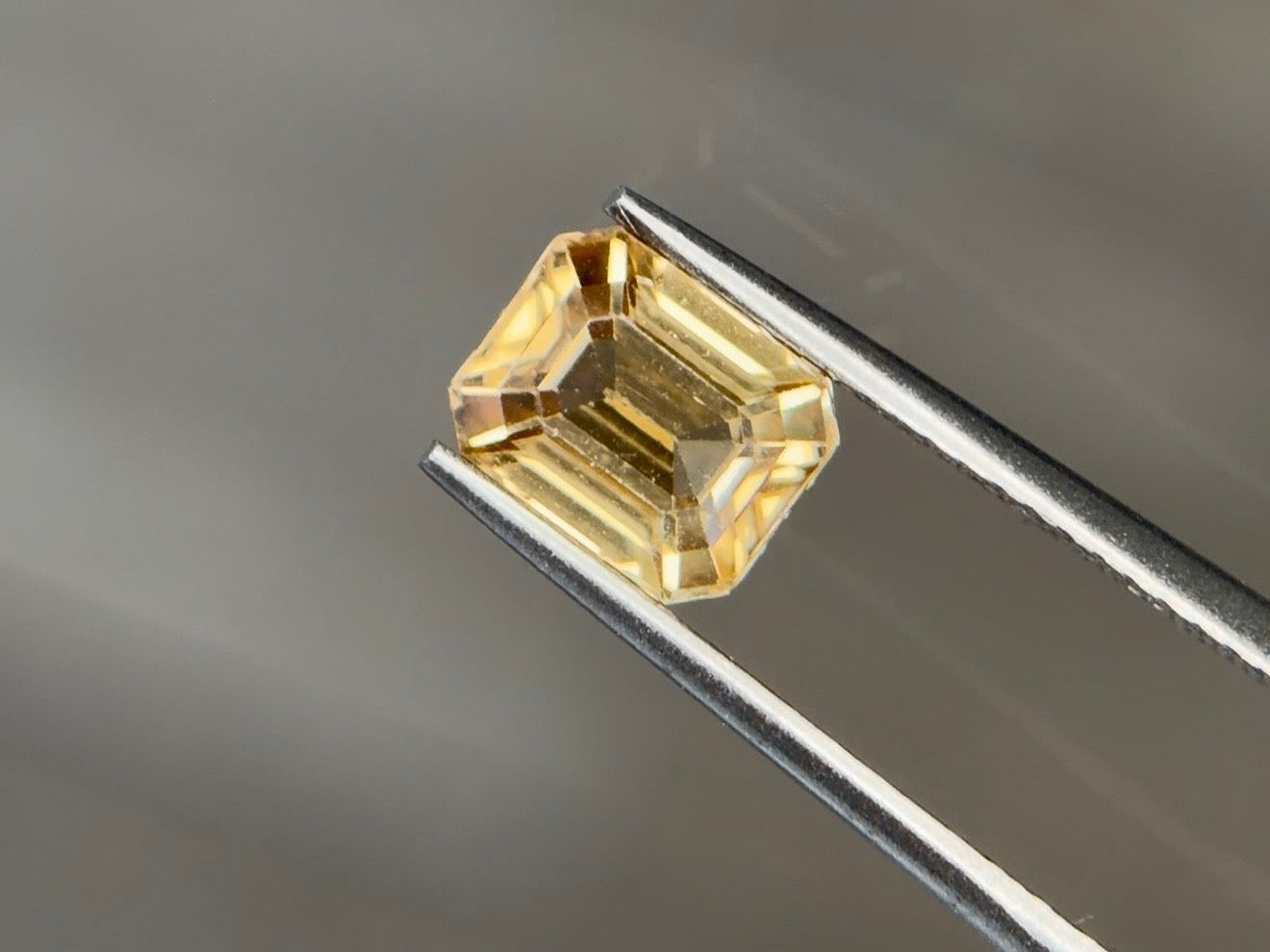 Medium slightly brownish to orangy yellow natural zircon in a 1.97 carat octagon step cut, held in tweezers against a warm gray background