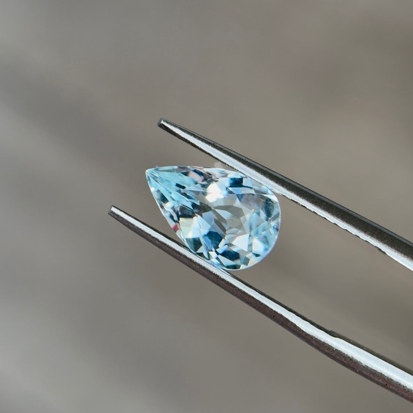 Pear-shaped aquamarine in light to medium slightly greenish blue held in tweezers, the modern March birthstone