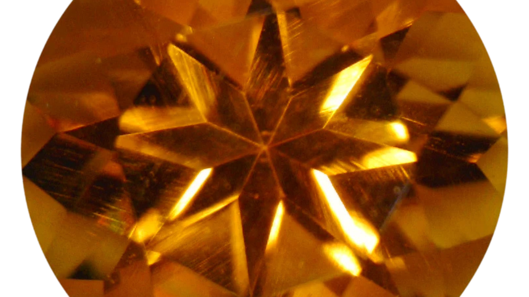 Round star-cut citrine in a vivid yellowish orange with a warm honey-gold core, photographed face-up on a pale gray background at Sapphire Row, its pinwheel facet pattern radiating from the culet