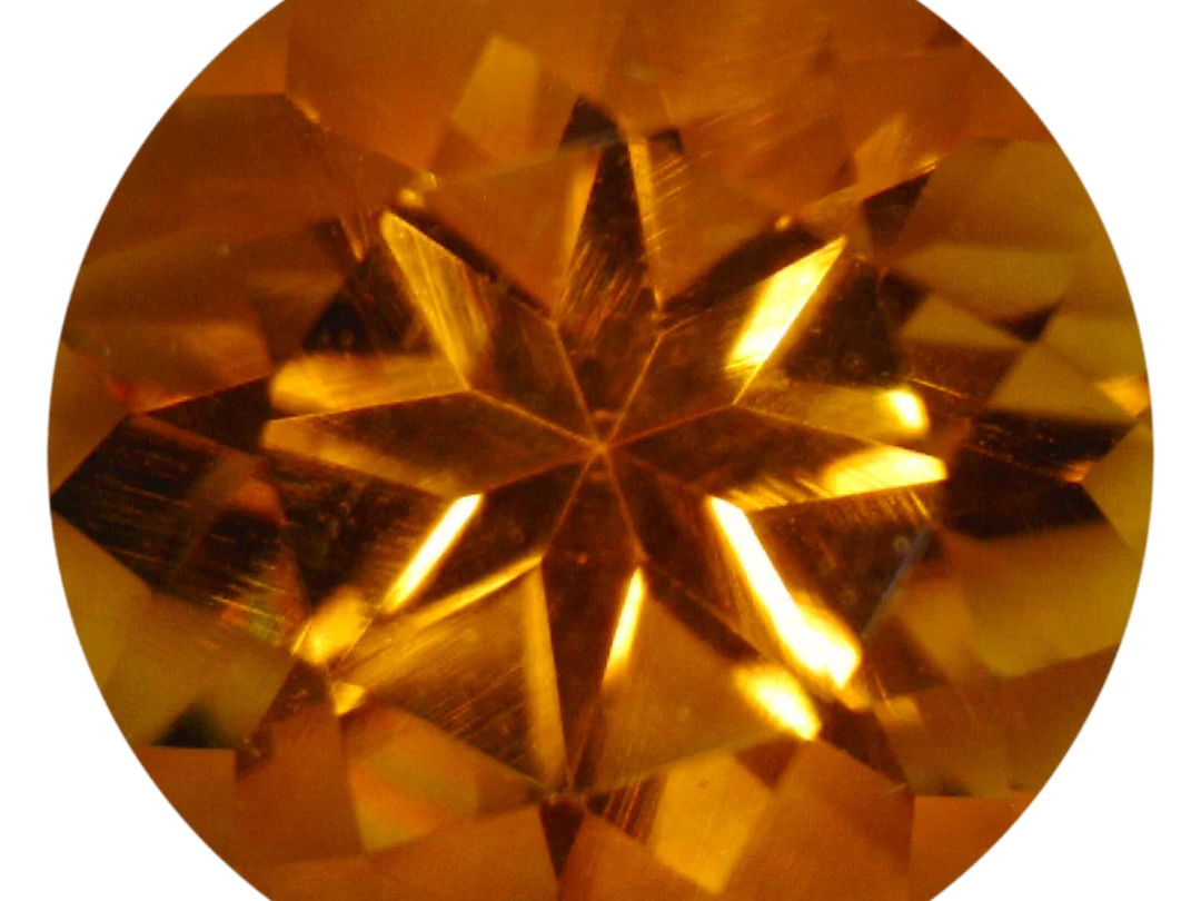 Round star-cut citrine in a vivid yellowish orange with a warm honey-gold core, photographed face-up on a pale gray background at Sapphire Row, its pinwheel facet pattern radiating from the culet