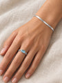 Natural Sky Blue Topaz Chain Ring in 14K White Gold, worn on the hand resting on ivory linen with a herringbone bracelet