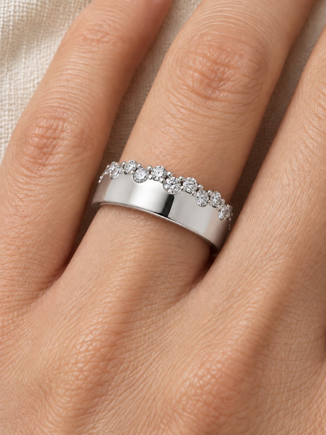 Natural Diamond Cigar Band in 14K White Gold, worn on the finger against ivory linen with staggered diamonds along the edge