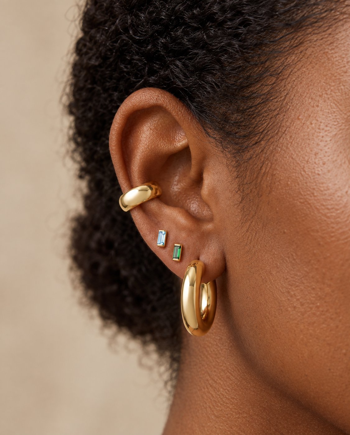 Lab-Grown Emerald Channel-Set Baguette Stud Earrings in 14K Yellow Gold, worn on the earlobe between an aqua-blue stud and a polished gold hoop
