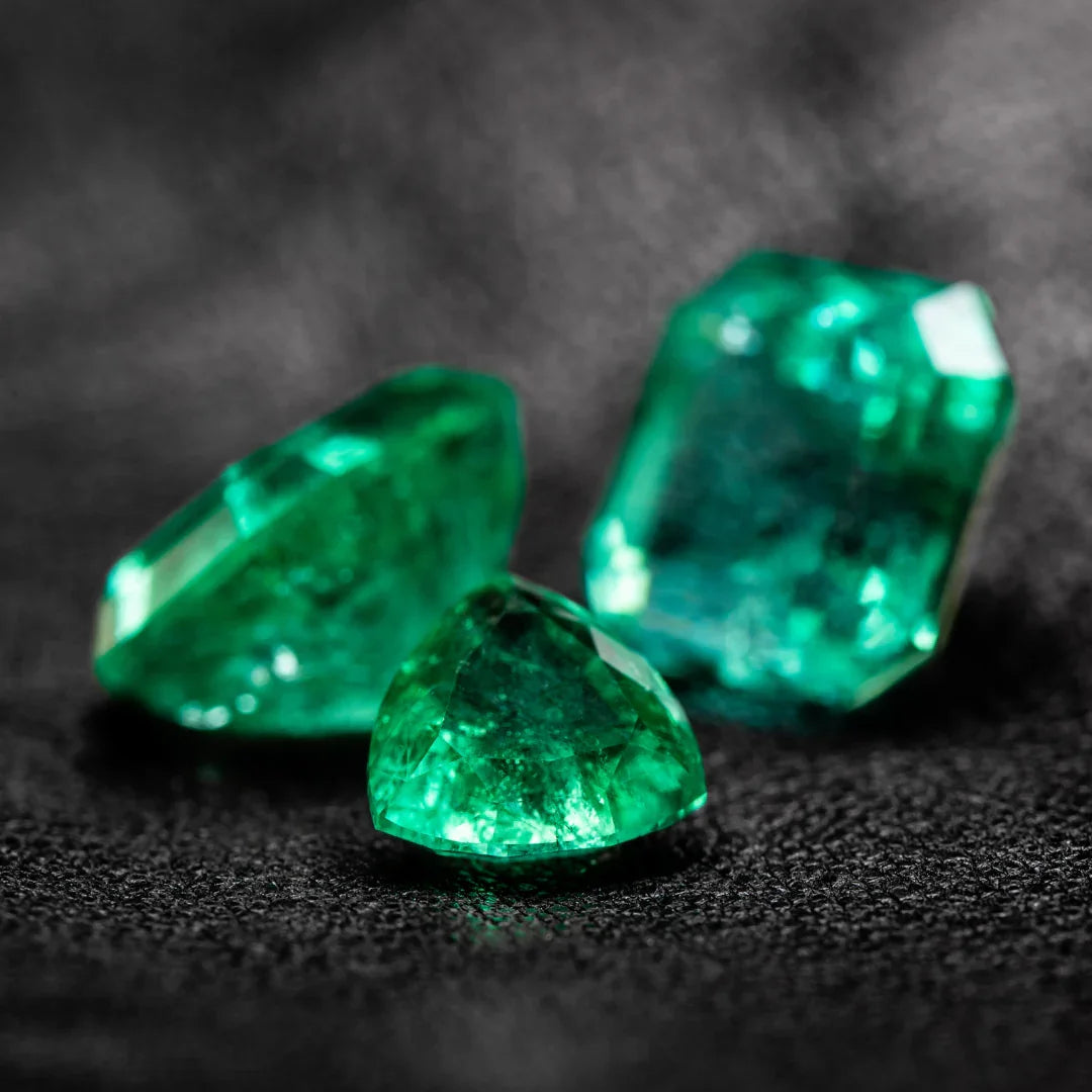 Three faceted green emerald gemstones on a textured black background