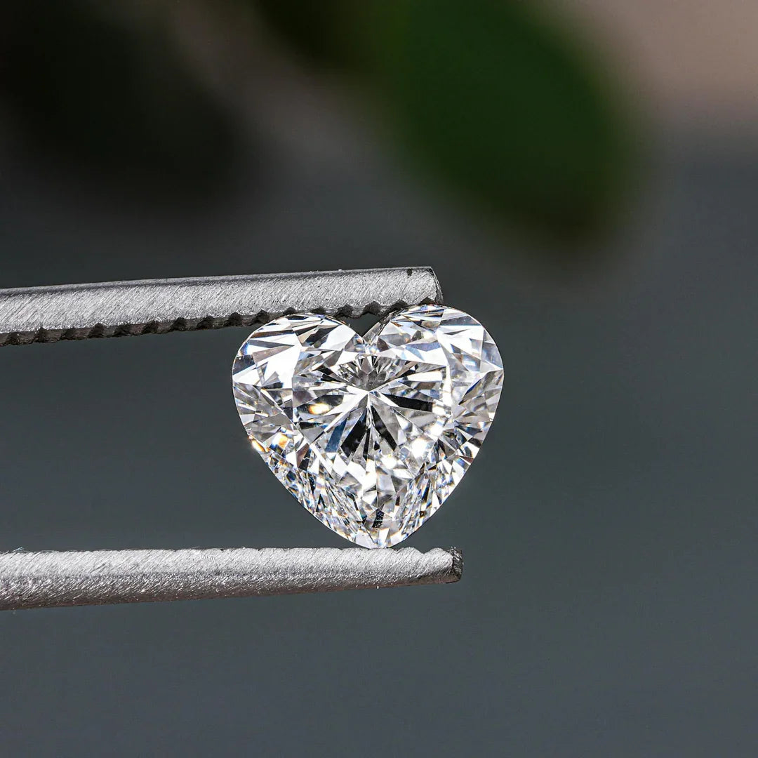 Heart-shaped faceted gemstone held by tweezers, sparkling against a neutral background.