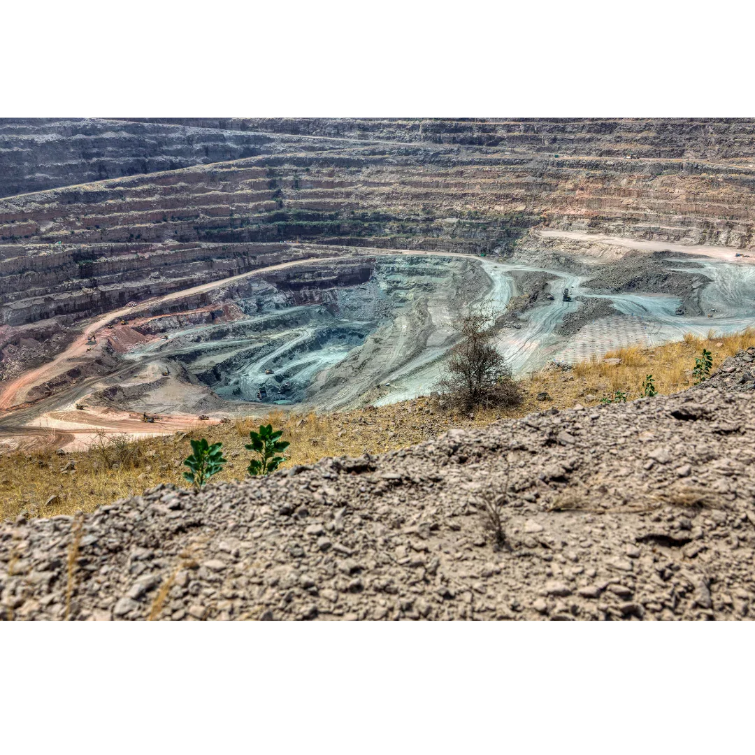 Open-pit gemstone mine with terraced rock layers and mining equipment in a dry landscape.
