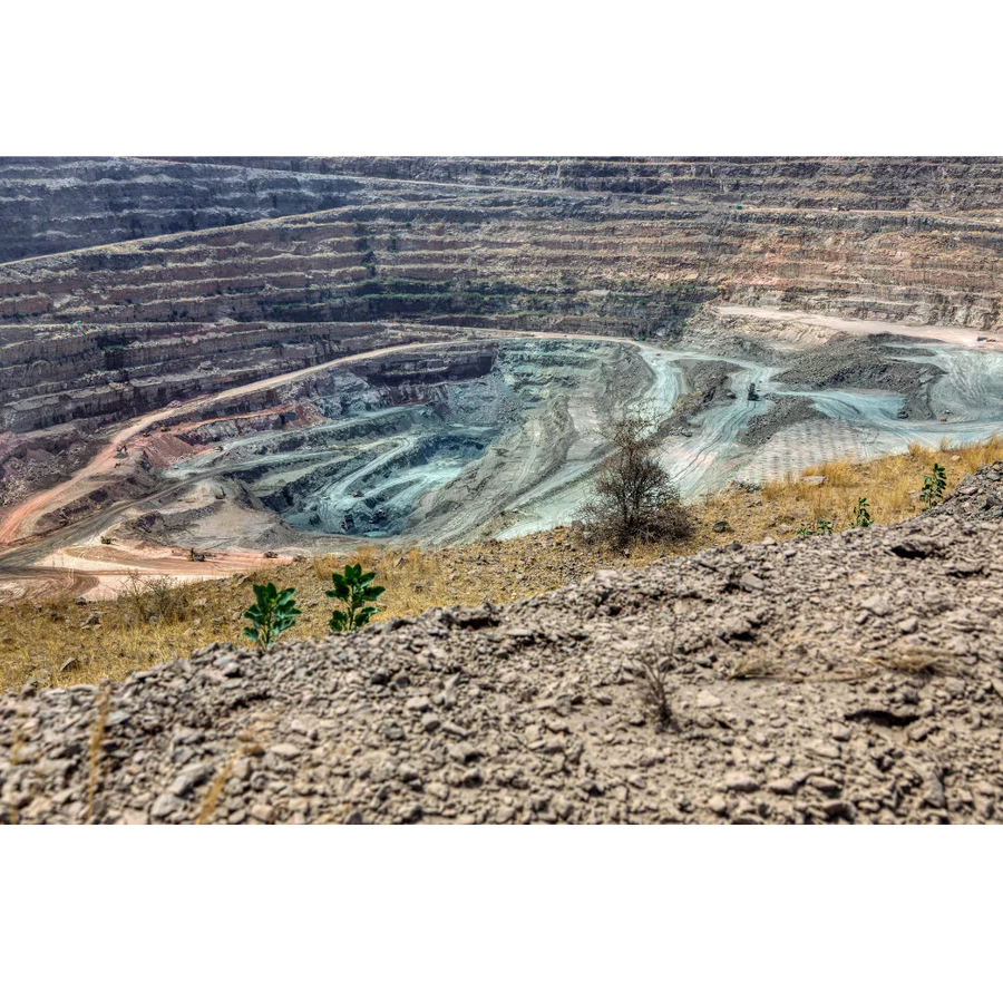 Open-pit gemstone mine with terraced rock layers and mining equipment in a dry landscape.