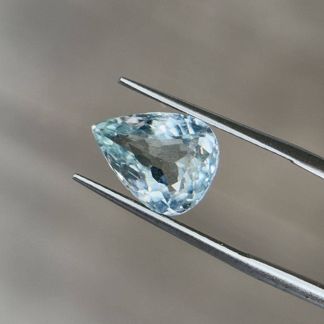 Pear-cut aquamarine gemstone face up in tweezers