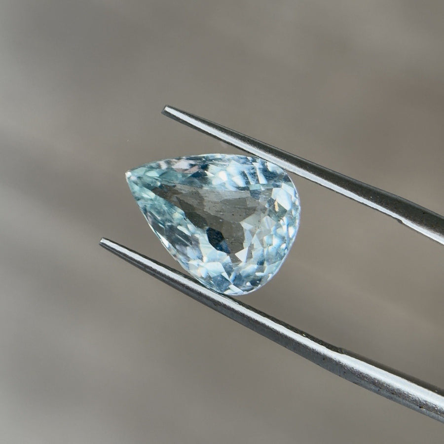 Pear-cut aquamarine gemstone face up in tweezers