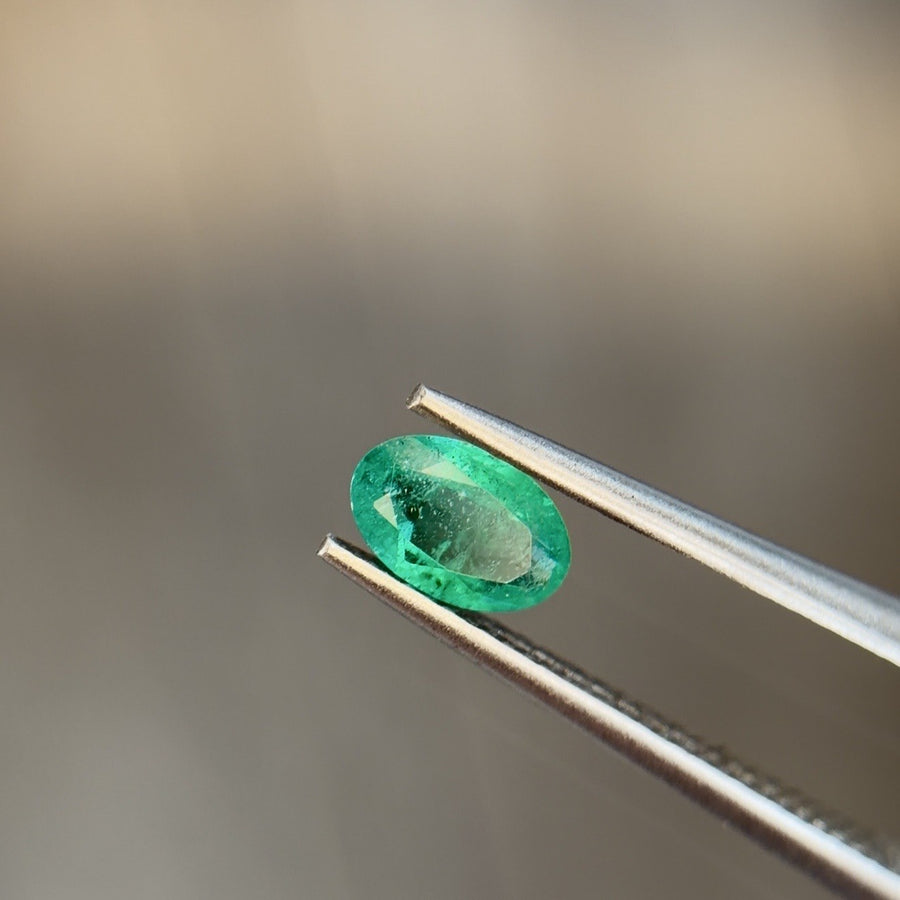 Oval natural emerald gemstone held in tweezers