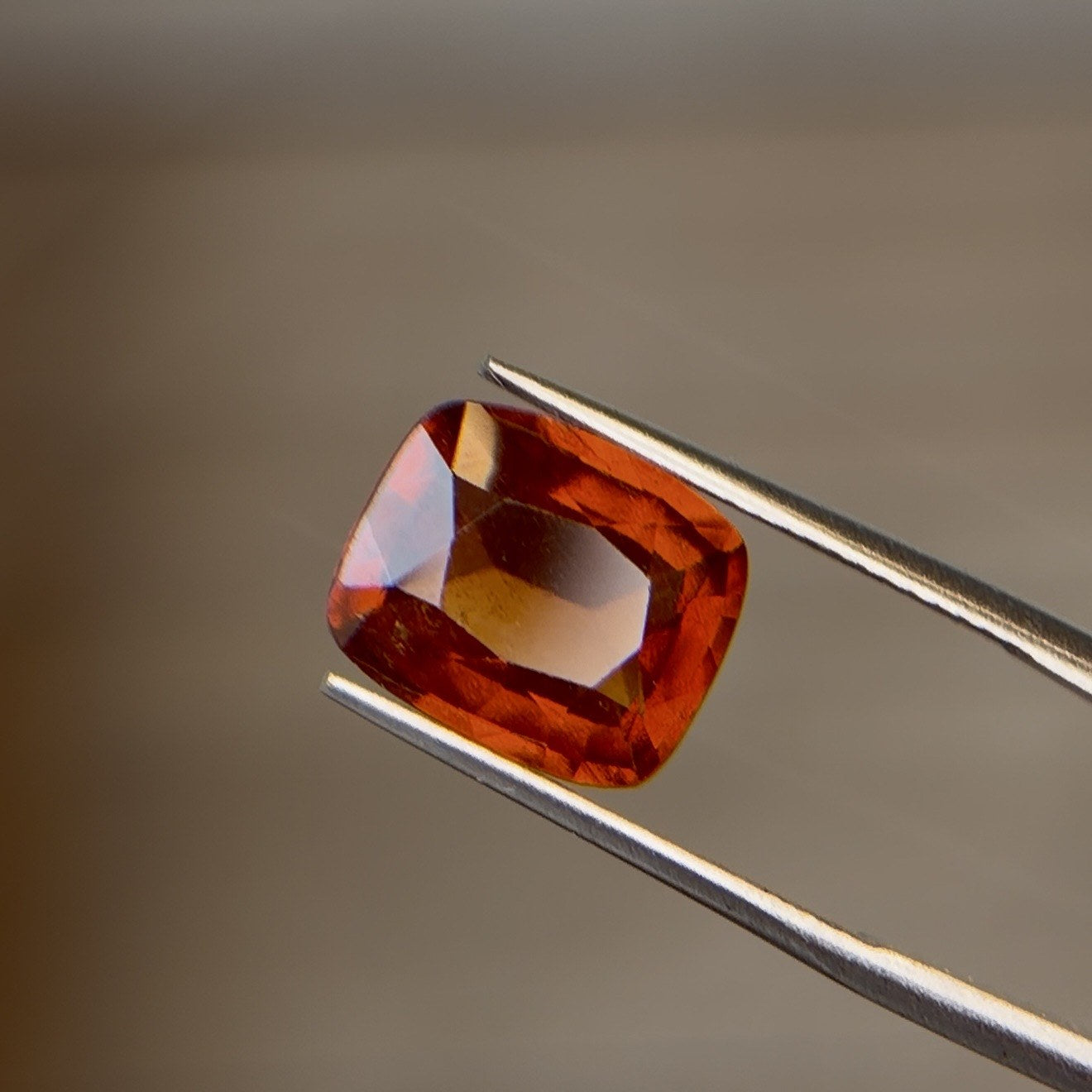 Cushion-cut orange garnet gemstone held in tweezers