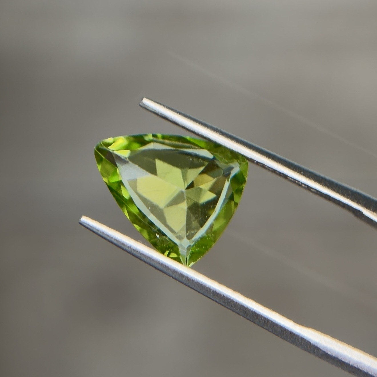 Trillion-cut natural peridot gemstone held in tweezers