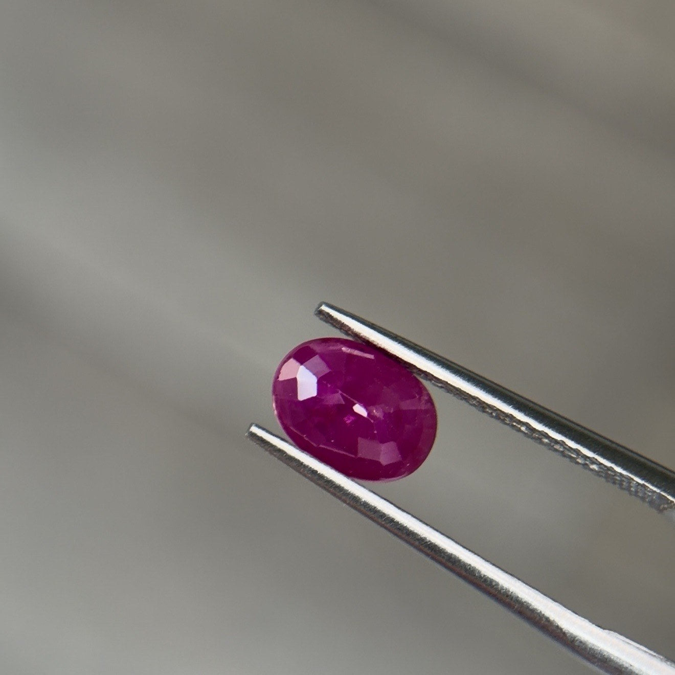 Oval rubellite tourmaline gemstone held in tweezers