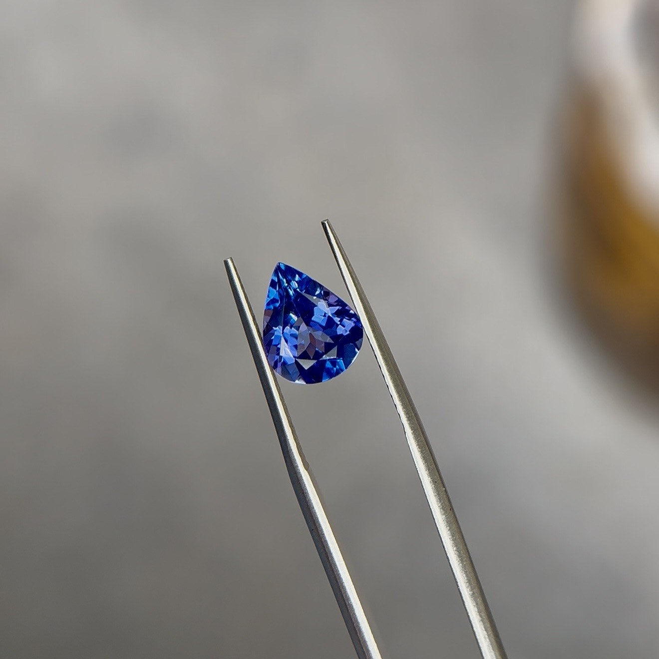 Pear-cut violet-blue tanzanite gemstone face up in tweezers