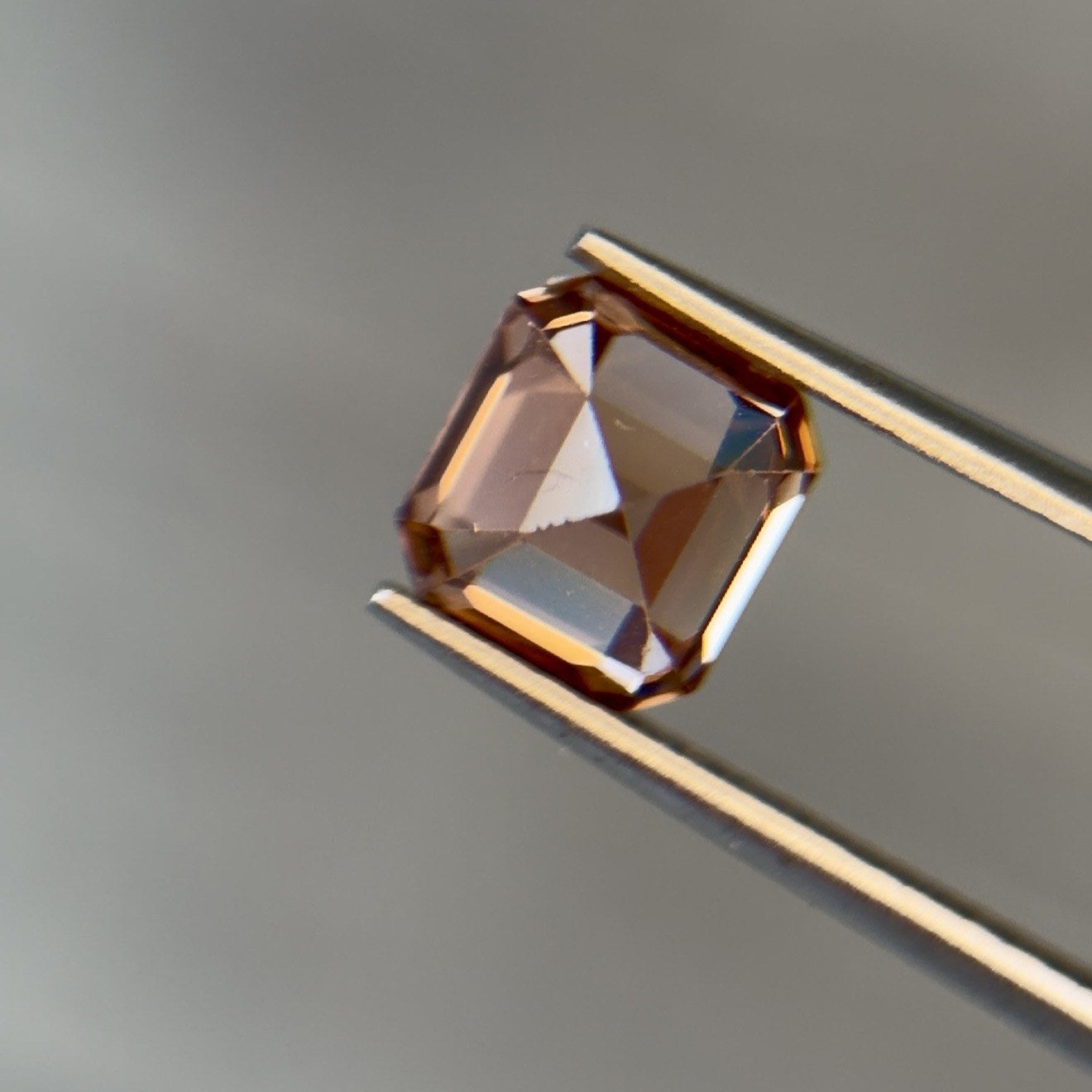 Cognac-colored natural zircon gemstone held in tweezers
