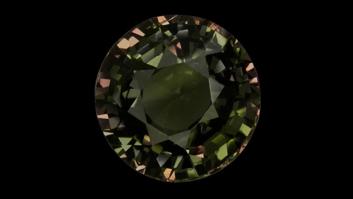 Round alexandrite gemstone with green-to-red color change on a black background
