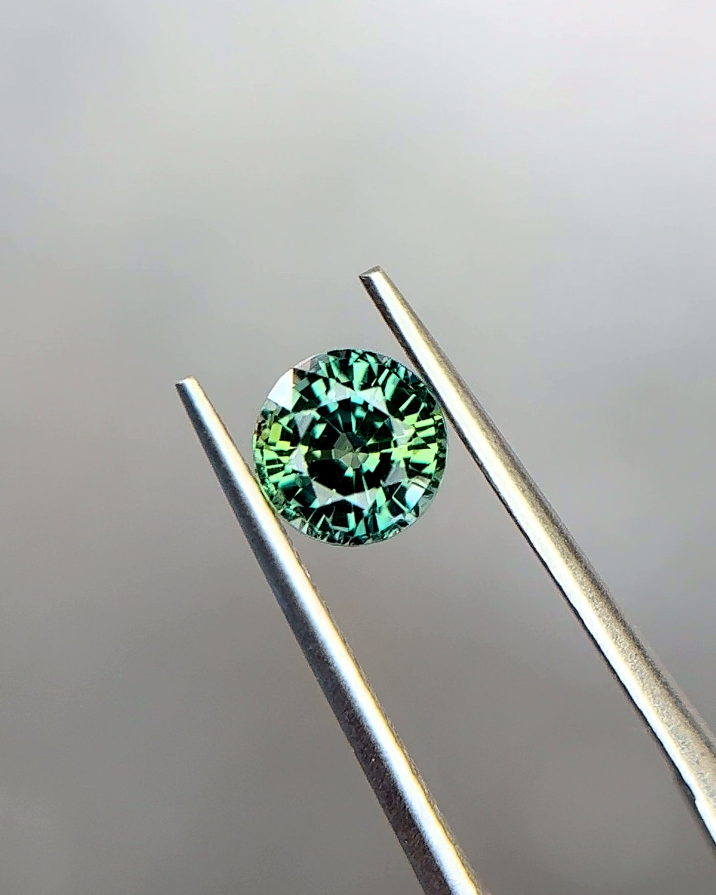 1.09 ct natural teal-green parti sapphire from Tanzania, round cut, held in tweezers