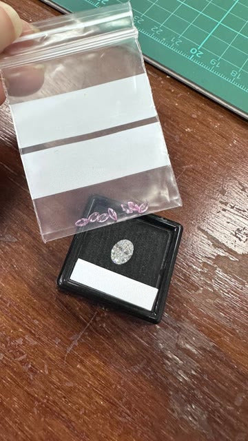 The oval diamond in its box and the pink sapphires in a bag
