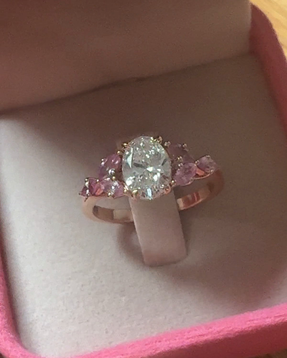 The finished oval diamond ring with pink sapphires in rose gold, in its box