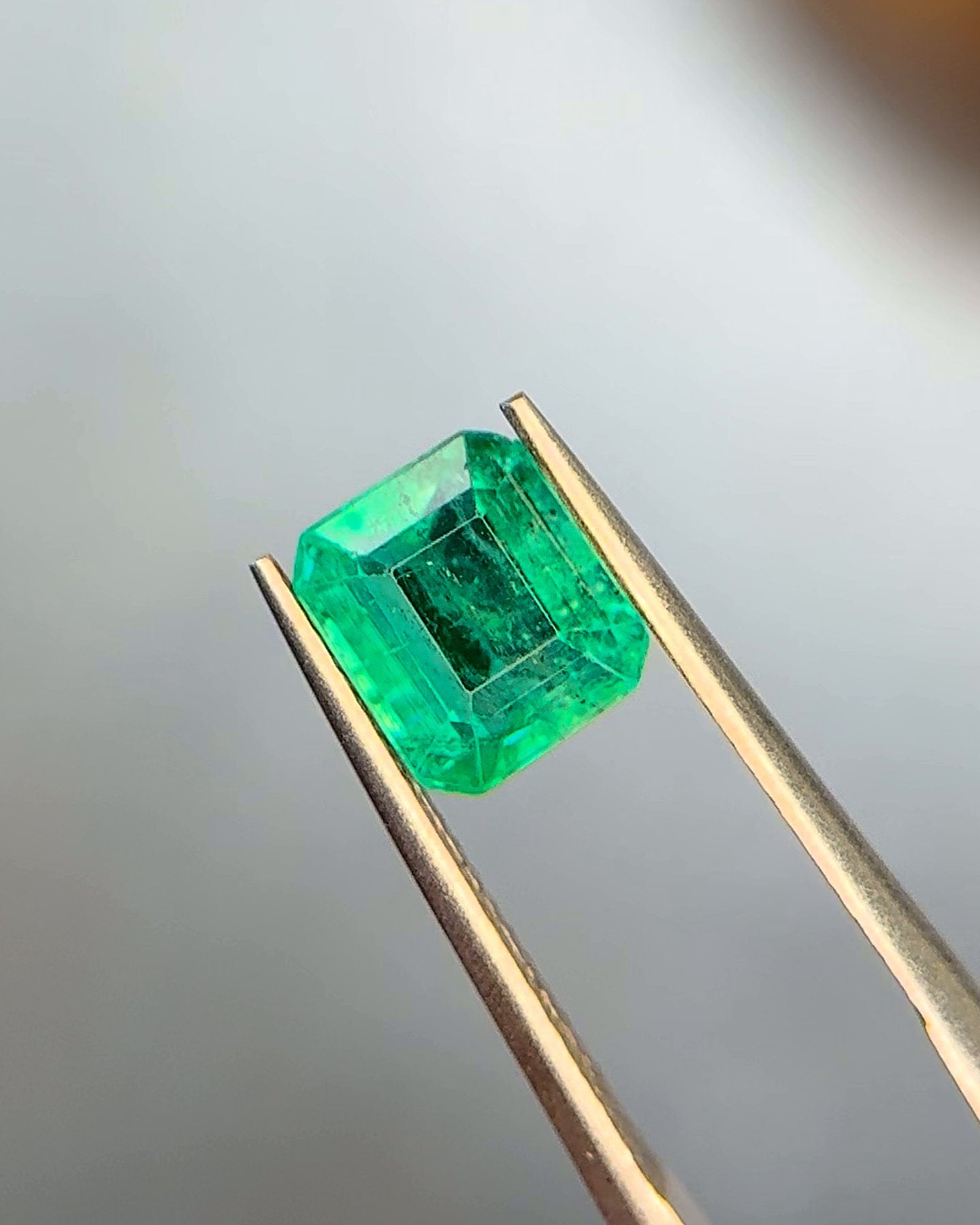 A vivid bluish-green emerald held in tweezers